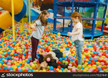 Children with mother lying among colorful balls in the entertainment center. Mom and her daughter leisures on holidays, childhood happiness, happy kids on playground. Children with mother lying among colorful balls