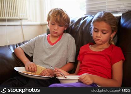 Children With Poor Diet Eating Meal On Sofa At Home