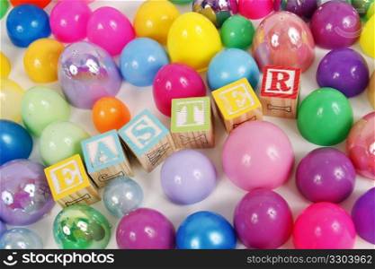 Childrens blocks spell Easter with colorful plastic eggs on a white background.