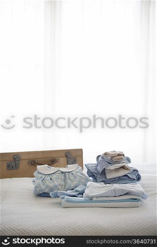 Childrens clothes folded on bed next to suitcase