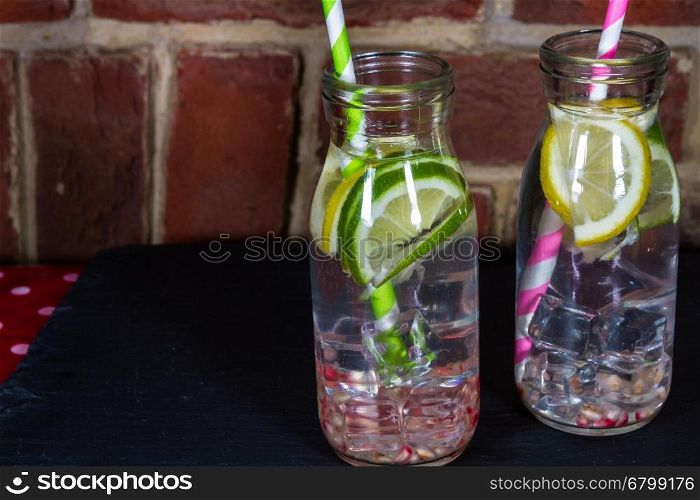 Childrens healthy water with ice, lemon, lime, pomegranate seeds and straws.