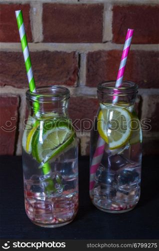 Childrens healthy water with ice, lemon, lime, pomegranate seeds and straws.