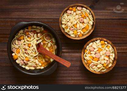 Chilean traditional Porotos con Riendas (beans with reins) dish of cooked dried beans with pumpkin, onion, spaghetti and sausage, in rustic bowls, photographed overhead on dark wood with natural light