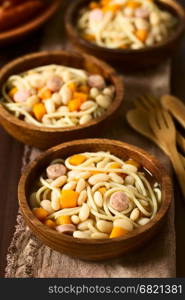 Chilean traditional Porotos con Riendas (beans with reins) dish of cooked dried beans with pumpkin, onion, spaghetti and sausage, in wooden bowls, photographed on dark wood with natural light (Selective Focus, Focus in the middle of the first dish)