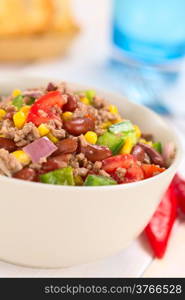 Chili con carne salad made of mincemeat, kidney beans, green bell pepper, tomato, sweet corn and red onions served in bowl with chili on the side (Selective Focus, Focus in the middle of the salad)