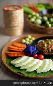 Chili paste paste in a bowl with eggplant, carrots, chili, cucumbers in a basket on wood table