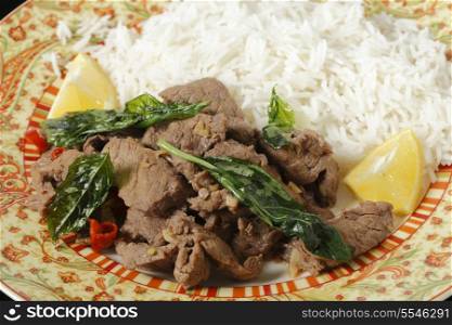 Chilli beef with crispy fried basil leaves, served with white basmati rice and lemon wedges.