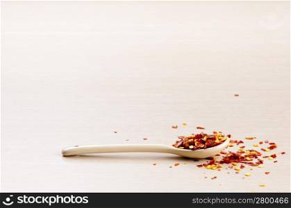 Chilli Flakes in a spoon with some spilt over the wooden background