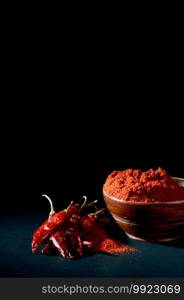 chilly powder in wooden bowl with red chilly, dried chillies on black background