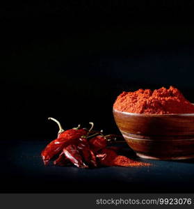 chilly powder in wooden bowl with red chilly, dried chillies on black background