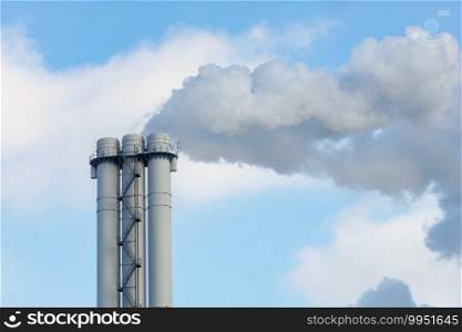 Chimney against the background of clear sky, the concept of saving the atmosphere and the environment from pollution and emissions, copy space.. Emissions of smoke and steam from an industrial chimney into a clear sky.