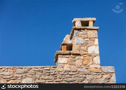 Chimney on home roof top made of old stone bricks against blue sky.. Stone amde chimney on roof
