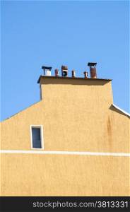 Chimney section of yellow house wall with different chimney caps on blue sky background