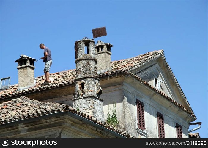Chimney sweep on the tile roof of old house
