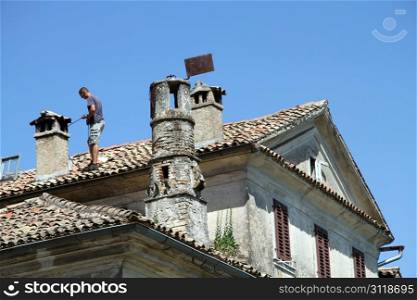 Chimney sweep on the tile roof of old house