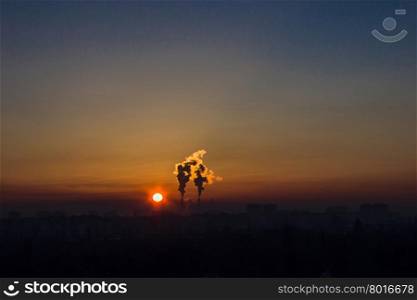 Chimneys and dark smoke over factory at sunset