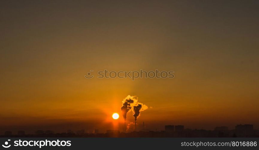 Chimneys and dark smoke over factory at sunset