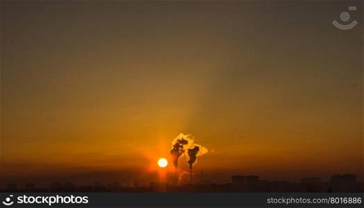 Chimneys and dark smoke over factory at sunset