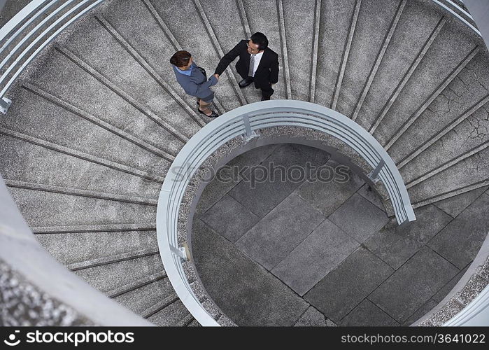 China, Hong, Kong, two business people shaking hands standing on spiral staircase, view from above