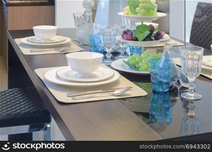 Chinaware setting on dining table with light blue crystal glass and fruits