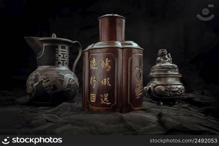 Chinese antique tea leaf iron storage jar (Characters chinese is Name of the tea), Chinese antique teapot (Characters chinese is Double Happiness) and Silver antique incense burner on dark background. Chinese traditional style, Copy space, Selective focus.