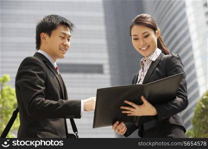 Chinese Businessman And Businesswoman Discussing Document Outside Office