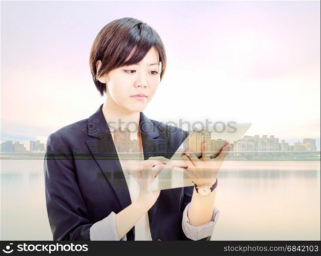 Chinese businesswoman in casual office clothes working on tablet computer with cityscape double exposure