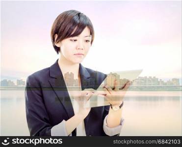 Chinese businesswoman in casual office clothes working on tablet computer with cityscape double exposure