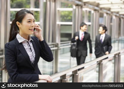 Chinese Businesswoman Outside Office On Mobile Phone With Colleagues In Background