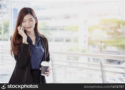 Chinese businesswoman using cellphone with smiling face call for business deal. Professional working woman wear black suit hold smart phone and talk wireless mobile technology concept.