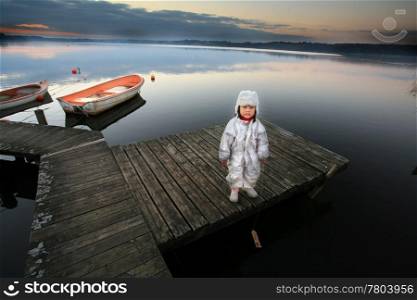 Chinese child with hat in winter looking at the cameraThe child stands in front of a lake and hold a small wooden boat