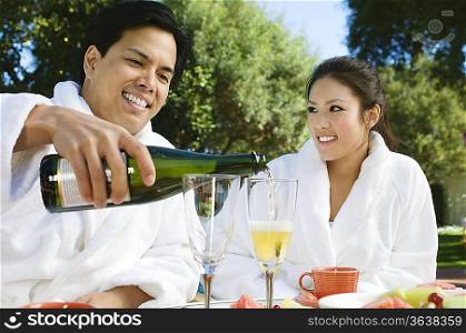 Chinese couple wearing bathrobes, drinking champagne at outdoor table