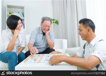 Chinese family playing Chinese chess at home, senior father with his adult son and daughter.
