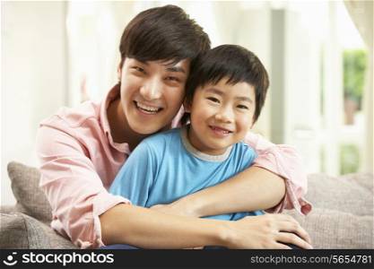 Chinese Father And Son Relaxing On Sofa At Home