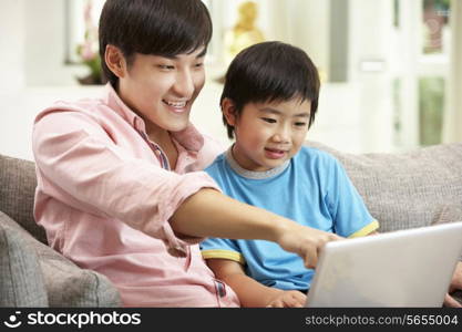 Chinese Father And Son Using Laptop Whilst Relaxing On Sofa At Home