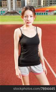 Chinese female jogger standing on sports field looking at camera