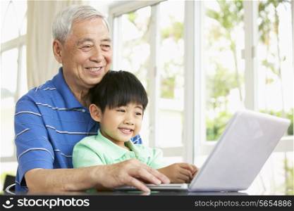 Chinese Grandfather And Grandson Sitting At Desk Using Laptop At Home