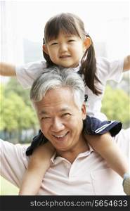 Chinese Grandfather Giving Granddaughter Ride On Shoulders In Park