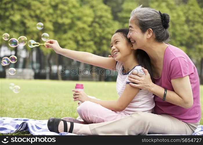 Chinese Grandmother With Granddaughter In Park Blowing Bubbles