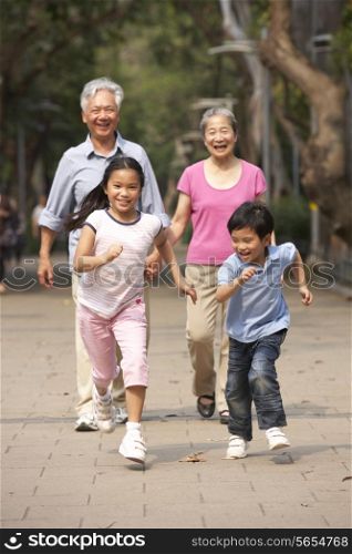 Chinese Grandparents Walking Through Park With Running Grandchildren