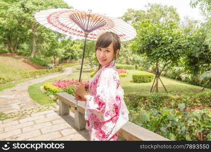 Chinese lady wearing kimono and holding umbrella in traditional Japanese style garden