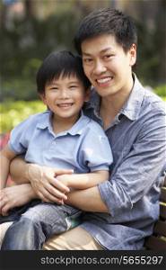 Chinese Man With Son Relaxing On Park Bench