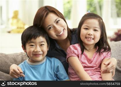 Chinese Mother And Children Sitting On Sofa At Home Together