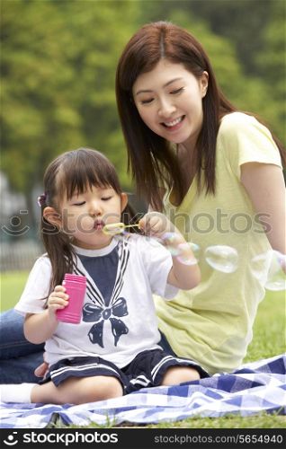 Chinese Mother With Daughter In Park Blowing Bubbles