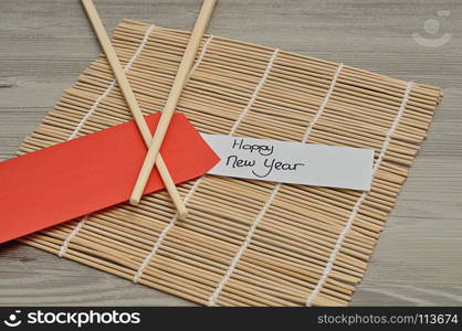 Chinese New Year design. A red envelope for money in the Chinese New Year isolated on a bamboo background with chopsticks and a note Happy New year