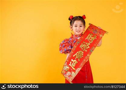 Chinese New Year. Happy Asian Chinese little child girl smile wearing red cheongsam qipao Spring festival couplets  Character  FU  means fortune, blessing , studio short isolated on yellow background