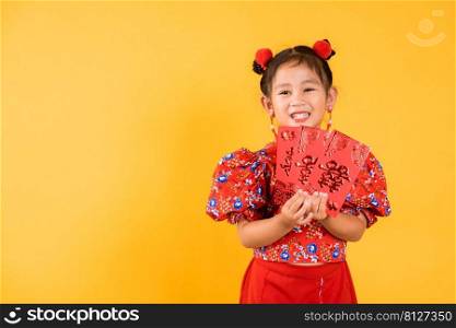 Chinese New Year. Happy Asian Chinese little girl smile wear red cheongsam qipao hold angpao red packet monetary gift, Portrait child in traditional dress, studio short isolated on yellow background