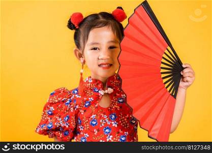Chinese New Year. Happy Asian Chinese little girl smile wearing red cheongsam holding fan, Portrait children in traditional dress, studio short isolated on yellow background