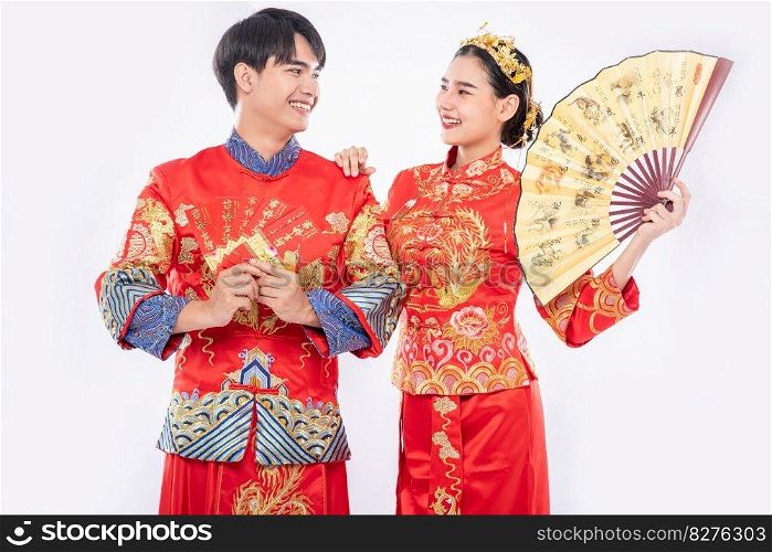 Chinese new year, man and woman wear cheongsam smiling to welcome good thing with gift money and hand fan