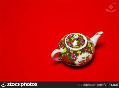 Chinese porcelain jug for tea and coffe with painted colorful flowers on an isolated red background.Horizontal view.